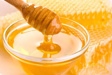 Golden raw honey dripping from a wooden dipper into a bowl