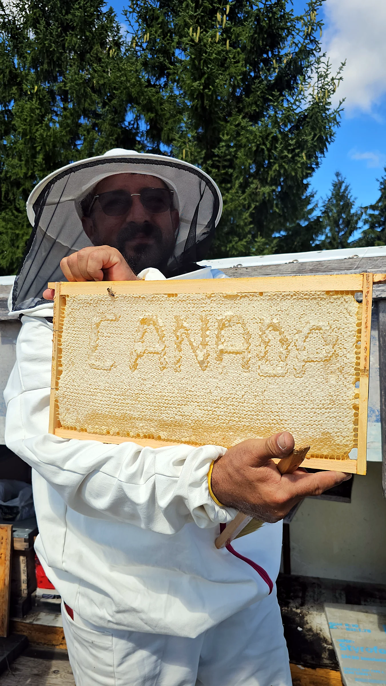 Beekeeper holding a honeycomb in which the word CANADA is formed by the cells of the comb